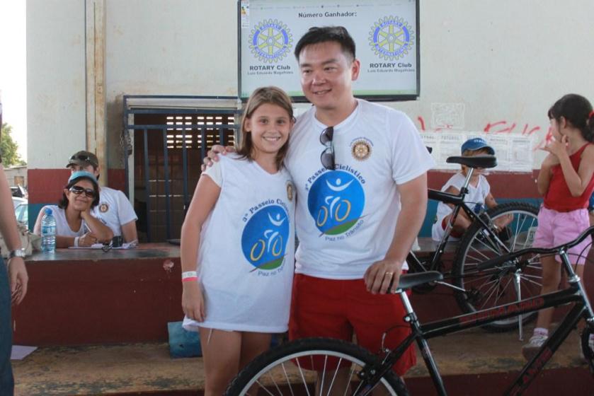 A sortudinha ganhadora de uma bicicleta, junto com o presidente Reginal Arita